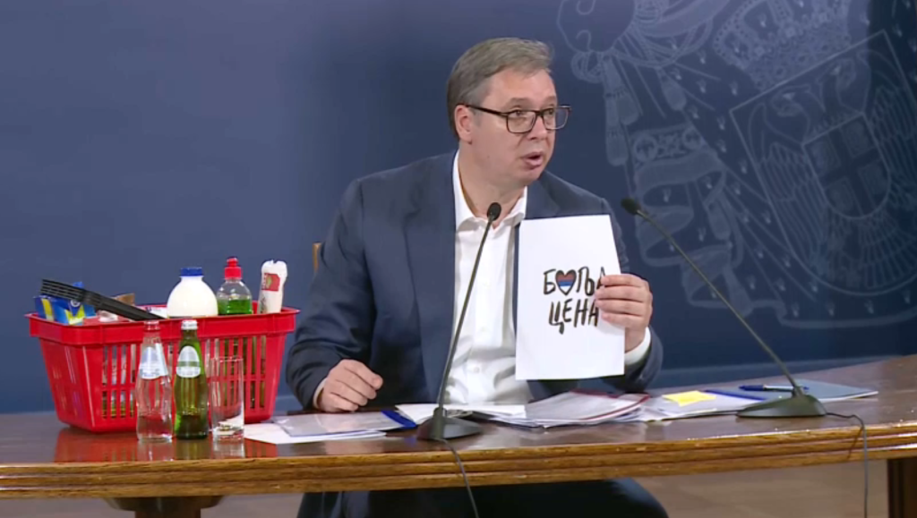 Aleksandar Vučić drži logo "Bolja cena" dok predstavlja proizvode na boljolj ceni.
